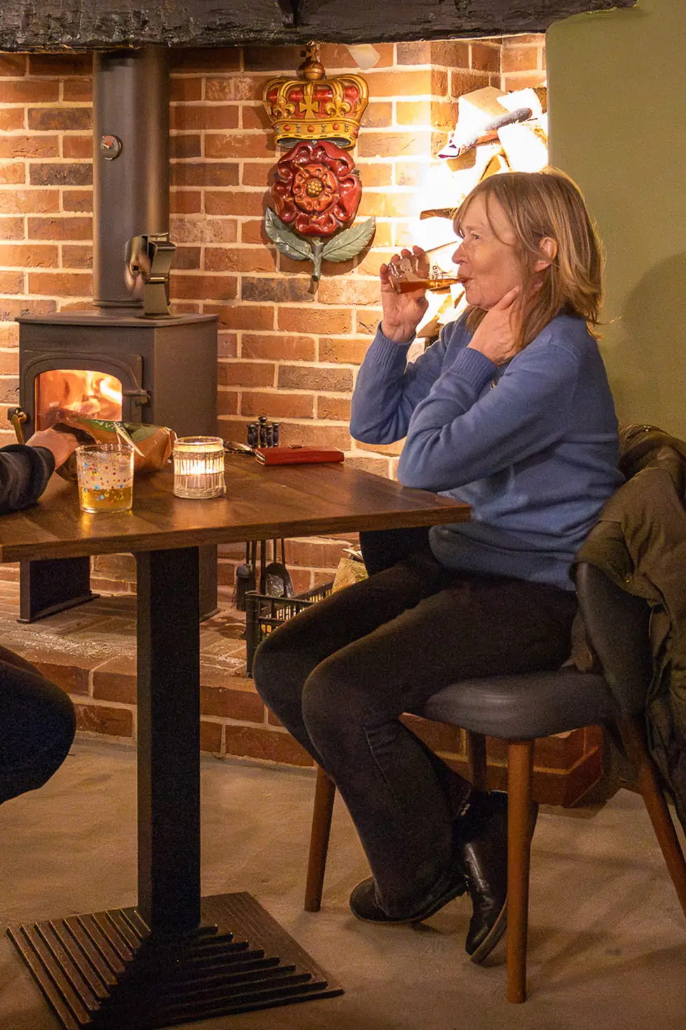 A guest enjoying a drink by the wood burner at the Rose & Crown